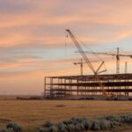 A prairie landscape at golden hour with cranes and steel framework of a data center under construction