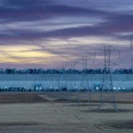 Power lines at dusk leading to a data center on farmland, AI-generated illustration